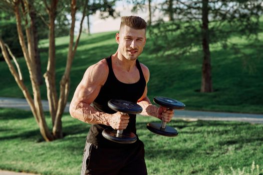 athletic man in black t-shirt with dumbbells in the park training. High quality photo