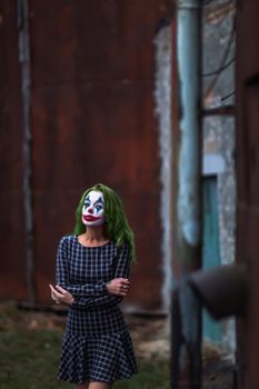 Portrait of a greenhaired girl in chekered dress with joker makeup on a atmospheric rusty metal wall background.