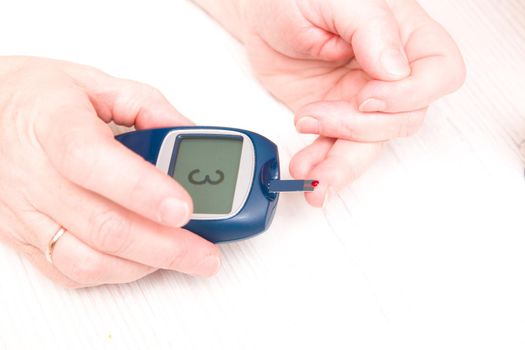 woman raised a finger with a drop of blood to measure blood sugar to a glucose meter, diabetes concept