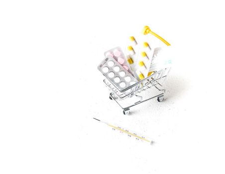 syringe, pills in a shopping trolley and mercury thermometer on a white background copy space