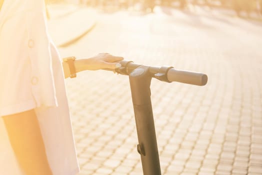 Unrecognizable young woman standing with an electric scooter in street on sunny summer day.