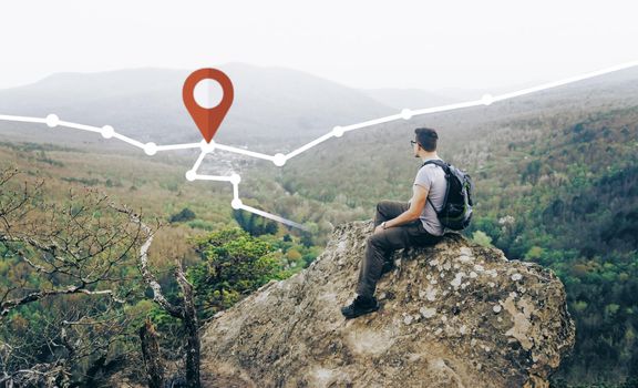 Hiker backpacker young man sitting on peak of rock and looking at route with location GPS pin in the mountains outdoor. Navigation concept.