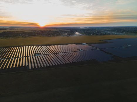 Aerial drone view into large solar panels at a solar farm in large field on countryside at bright sunset. Solar cell power plants, colorful photo