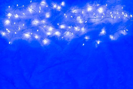 Christmas lights over a bright fluffy blue background. Yellow cozy christmas lights background. Modern scandinavian cozy new year background with copy space