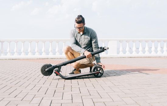 Young man folding an electric scooter in street outdoor.