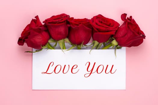 Love you banner. Red rose flowers arrangement with blank card on light pink background. Copy space. Top view