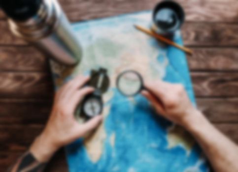 Man looking for a place to travel on map with magnifying glass, point of view. Image with blurred effect.