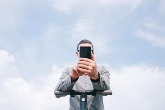 Young man with smartphone and an electric scooter outdoor, bottom view.