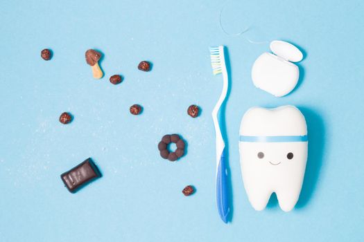 sweets, toothbrush, dental floss and toy tooth on a blue background, tooth model with a smile, protection of the oral cavity from caries concept, pediatric dentistry advertising