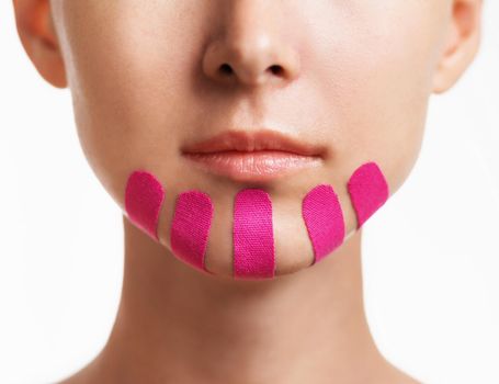 Young woman with vertical kinesio tapes on chin for facelift, front view. Anti-aging and beauty procedure.