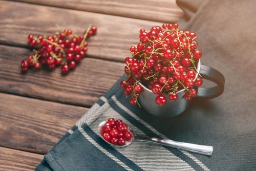 Fresh red ripe currant berries in a cup and on spoon on napkin on wooden table.