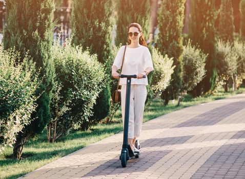 Modern girl riding an ecological electric scooter in summer park.