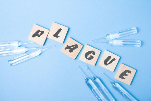 several glass ampoules and wooden squares with the inscription plague, plague 2020 concept, blue background, copy space, top view