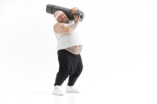 Happy fat man with big belly and tattos in sports wear with exercise mat