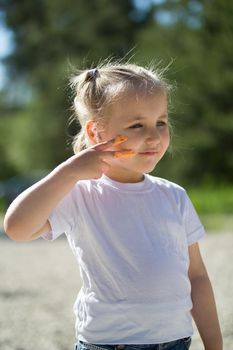 Cute little girl draws lines on the face with finger paints at summer vacation in park, close up