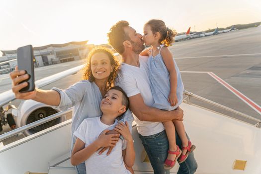 Smiling woman holding phone and making selfie of her family before flying on a plane. Travel concept