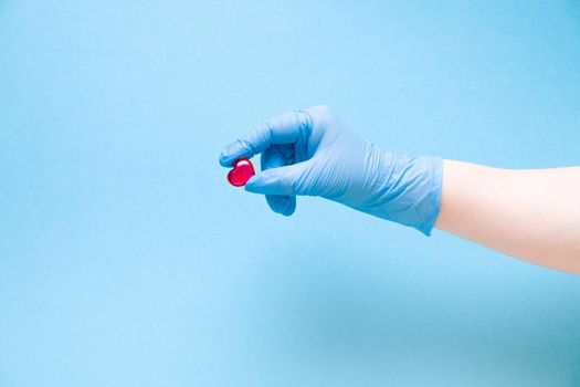 female hand in a blue disposable medical glove holds a small red glass center on a blue background, copy space, cardiology concept, health care and treatment and prevention of heart diseases