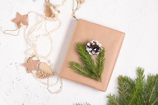 christmas gift box packed in kraft paper and decorated with a fresh spruce branch and a pine cone, natural materials for decorating gifts on a white background, eco friendly christmas concept
