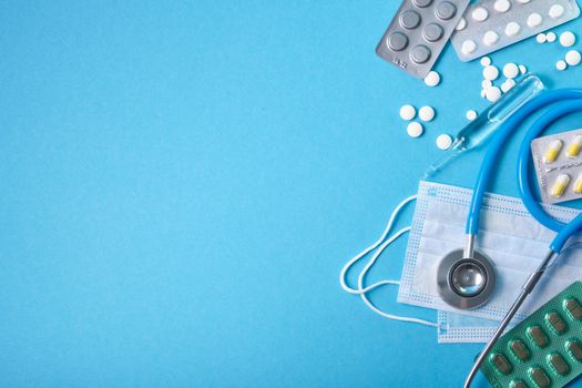 stethoscope, protective medical mask and various medications on a blue background copy space top view