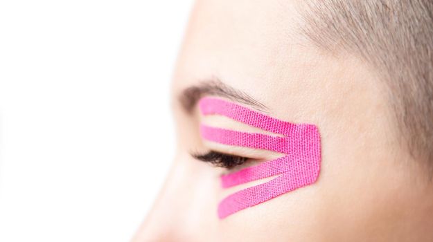 Young woman with applique of kinesiology tape on eyelid, side view close-up. Facelift and anti-aging beauty procedure.