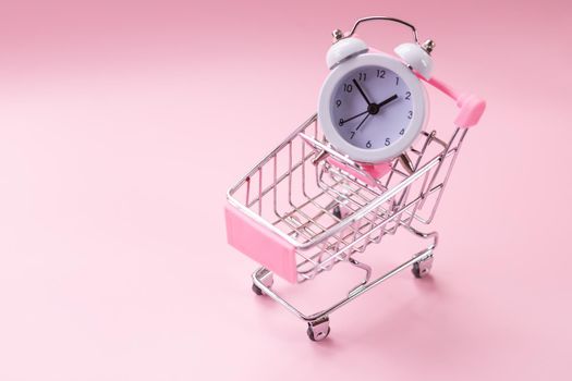 Black friday sale card in shopping cart and pink alarm clock on wooden background. Business concept.