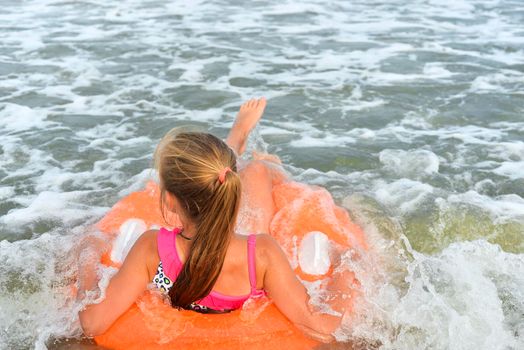 Child girl floatting on orange pool ring on the background of sea water and waves. Girl swimming on inflatable pool ring and looking at sea.