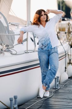 a happy woman with long hair stands on the pier near the yacht.