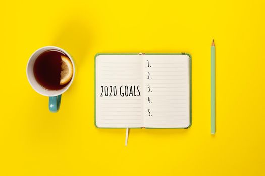 2020 goals banner. Notebook, pencil and cup of tea on a yellow background. Copy space, Flat lay.