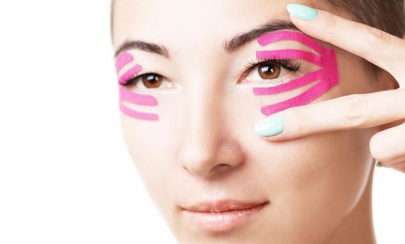 Smiling beautiful young woman with lifting kinesiology tape on eyelid.