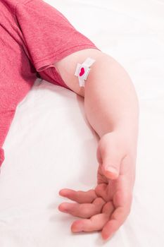 male hand with a patch glued with a cross on a white sheet, heart on a patch, blood donor concept