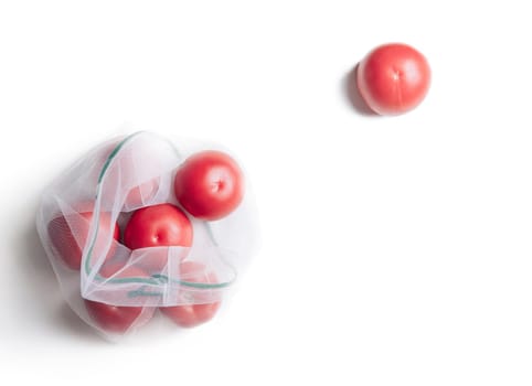 Reusable eco mesh bag with fresh ripe tomatoes on a white background, copy-space. Zero waste and no plastic concept.