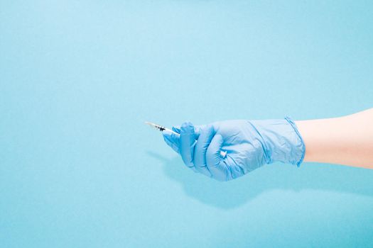 female hand in a blue rubber medical glove holds an insulin syringe on a blue background copy space, treatment and health care concept, diabetes concept