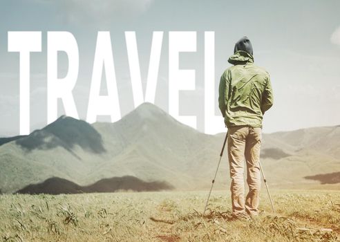 Explorer young man with trekking poles standing in front of word travel over mountain ridge in summer outdoor.