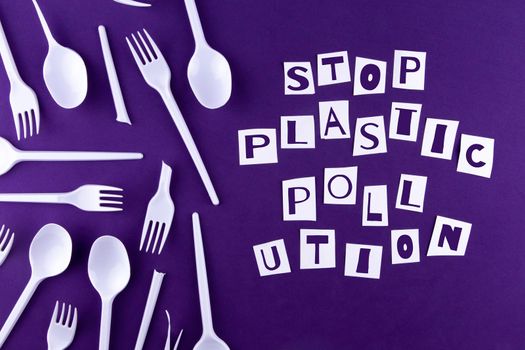 The word stop plastic pollution made of cut paper on a purple background with plastic utensils environmental pollution concept. Top view.