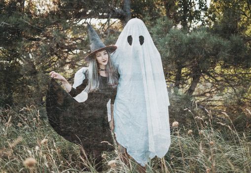 Couple wearing in costume witch and ghost standing in autumn forest outdoor. Theme of Halloween. Vintage image