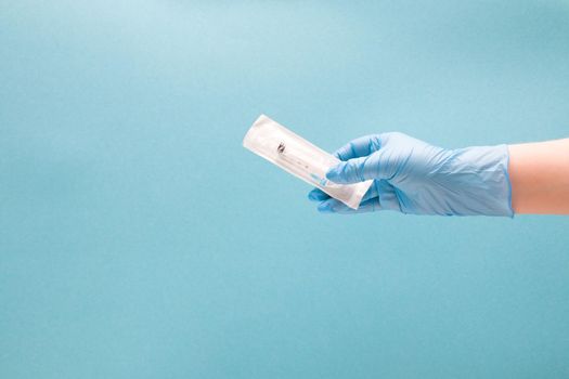 female hand in a blue disposable medical glove holds a disposable syringe in a package, blue background copy space