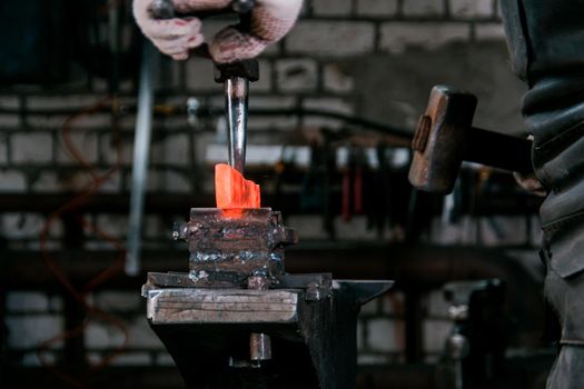 Workspace of blacksmith. Blacksmith working with red hot metal at anvil in a forge. Portrait