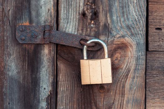 The old and vintage metal padlock with rust on the wooden door, locked for security