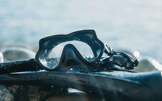 Equipment of freediver on pebble coast near the sea, mask and flippers with snorkel