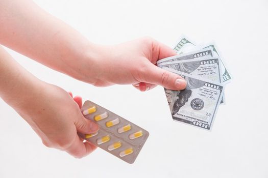female hands hold a pack of yellow and white pills capsules medicines and money dollar bills on a white background