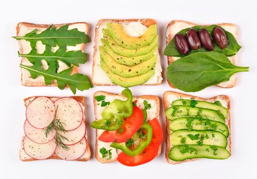 Set with toast bread and different vegan toppings on white background, top view. Toasts with avocado, spinach, arugula and other vegetables ingridients. Healthy snack or vegan food concept