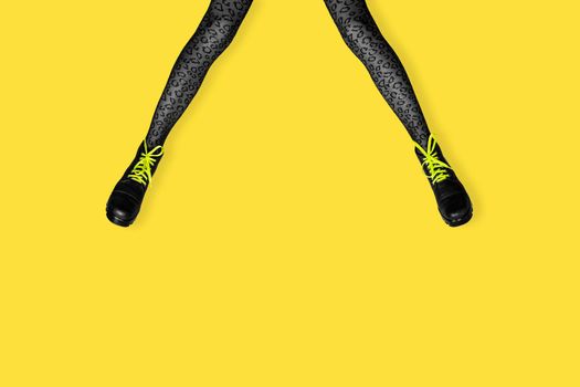 New gray female boots with bright yellow laces on long slender woman legs in gray tiger print tights isolated on yellow background. Pop art concept banner with copy space.
