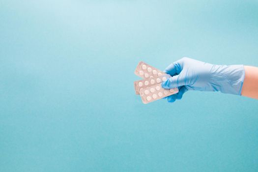 female hand in a blue disposable medical glove holds a fan three blisters with small white tablets on a blue background copy space