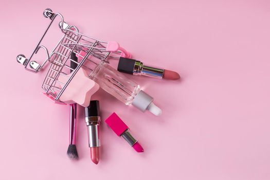 Shopping trolley with make-up products over white background