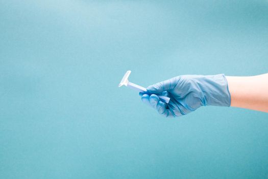 a female hand in a blue disposable medical glove holds a disposable blue razor, blue background copy space, shaving before surgery and medical intervention