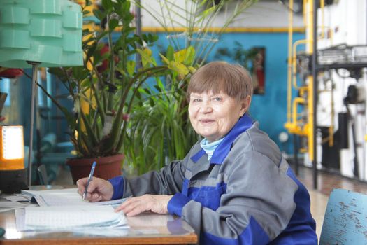 Elderly woman in workwear is writing on workplace, close up