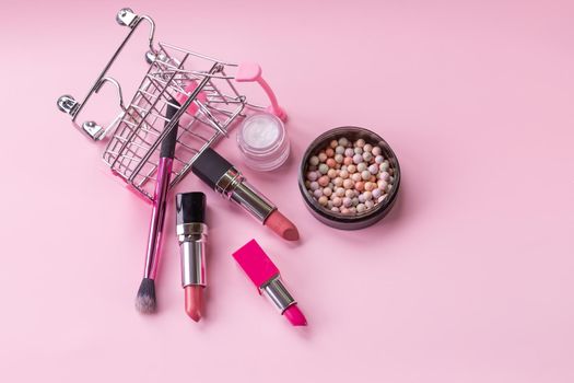 Creative concept with shopping trolley with makeup on a pink background.