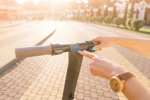 View of female hand turning on or off the electric scooter in summer park on sunny day.