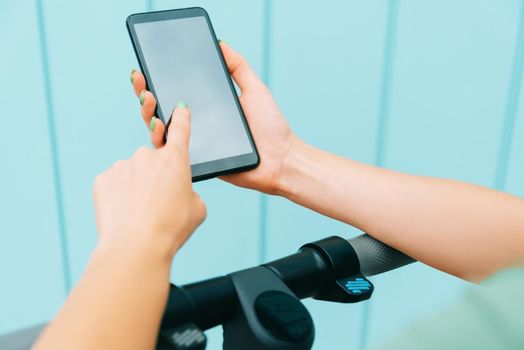 Woman texting message and using smartphone while standing with an electric scooter, mock-up. View of female hands with mobile phone.