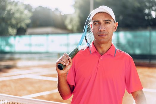 Middle-aged man tennis player with racket standing on tennis court near net